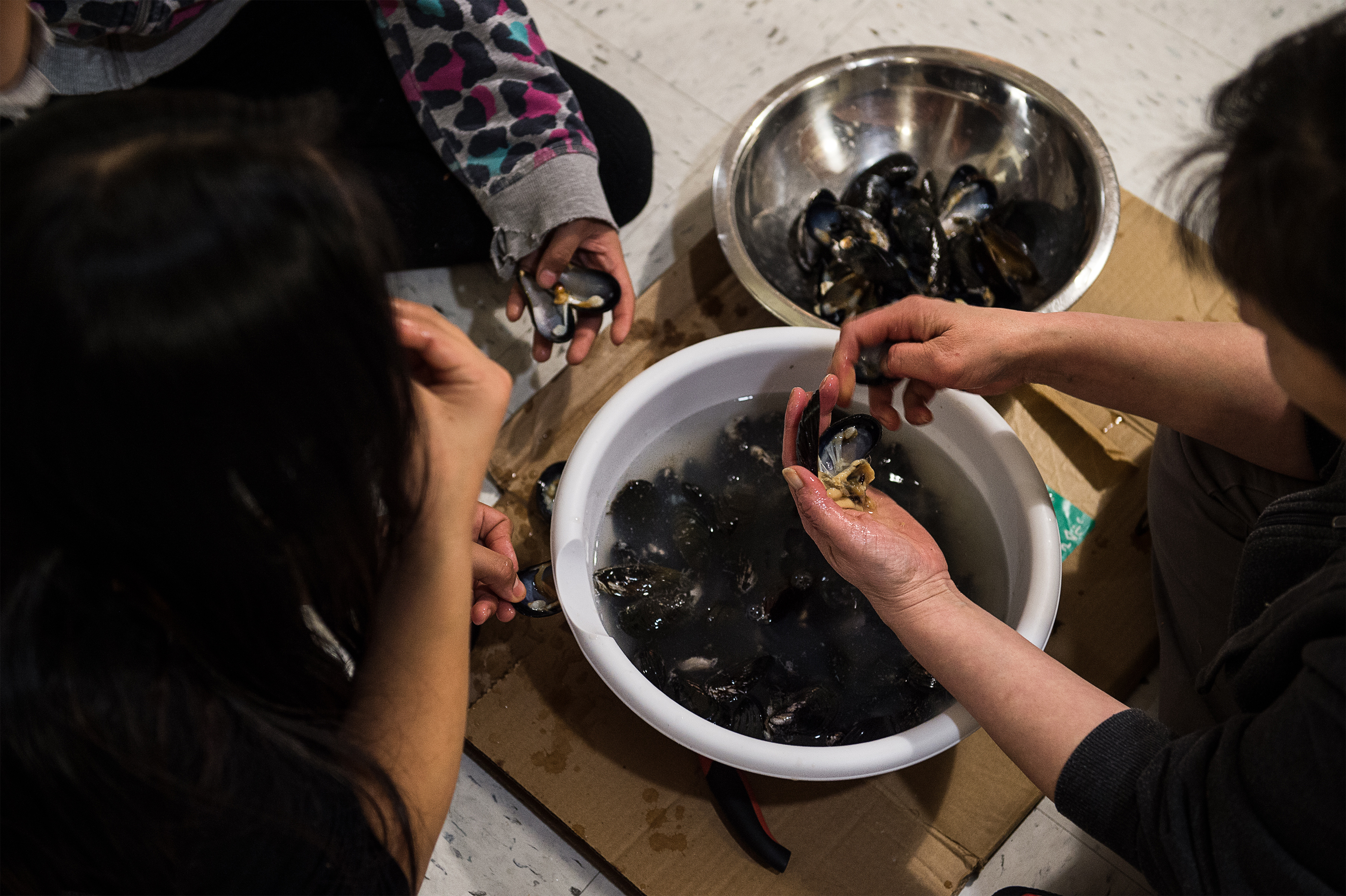 Siasi Qisiiq, right, Nayumik Qisiiq, center, and Annie Koniak eat raw mussels in Kangiqsujuaq, Nunavik, Quebec, March 2, 2017. When the winter tide goes out on a northern Canadian bay, some Inuit clamber into the ice caves below to harvest fresh food. (Aaron Vincent Elkaim/The New York Times)