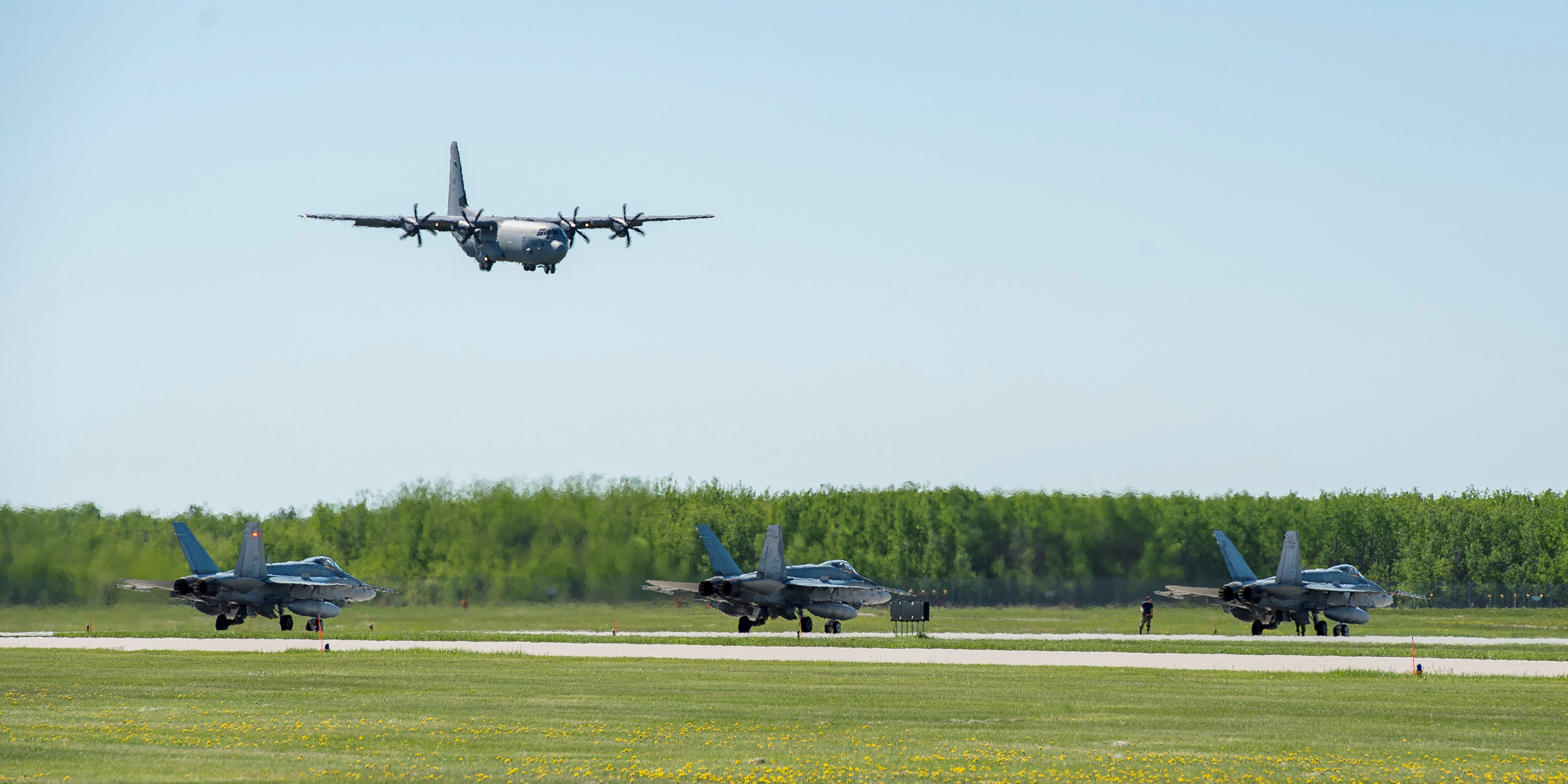 A Royal Canadian Air Force CC-130 Hercules starts its descent as three CF-188 Hornets sit on the tarmac during Exercise MAPLE FLAG 50 at 4 Wing Cold Lake, Alberta, Canada on May 29, 2017.  ( Justin Roy / Courtesy Canadian Armed Forces via Reuters)