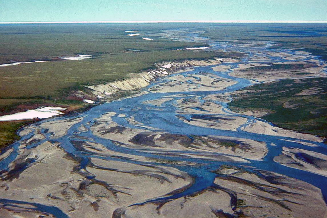 The Jago River flows north to the Arctic Ocean and its ice pack visible in the distance in the 1990s. Geologist Gil Mull said the yellowish gray weathering bluffs on the left had a strong gassy, oily odor on a warm day. (Gil Mull / Alaska Division of Geological and Geophysical Surveys)